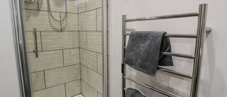 A bathroom with a glass shower enclosure, a towel rack with two towels, and a handheld showerhead.