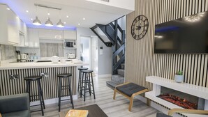 Et moderne køkken med en central ø, barstole, en pejs og en trappe til en etage ovenpå.