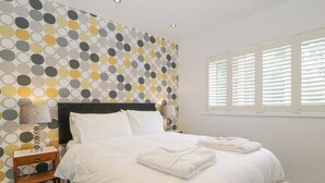 Een net opgemaakt bed met witte lakens, een houten hoofdbord en een muur met stippen.