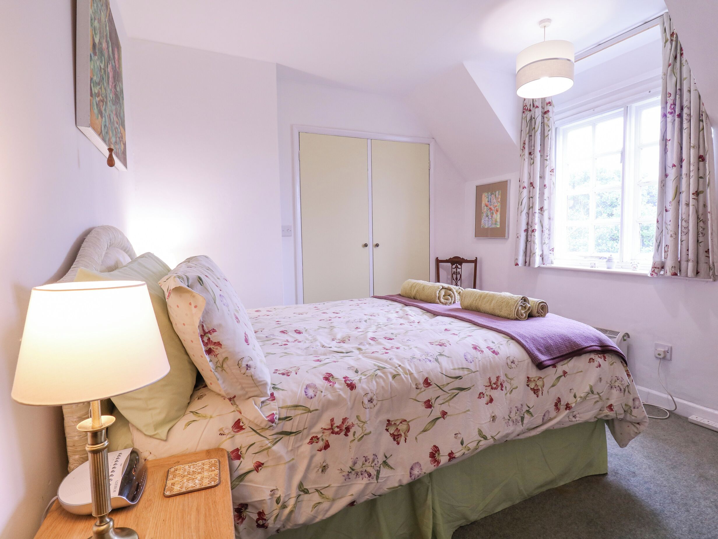 A bedroom with a bed, a nightstand, a lamp, a window with curtains, and a door.