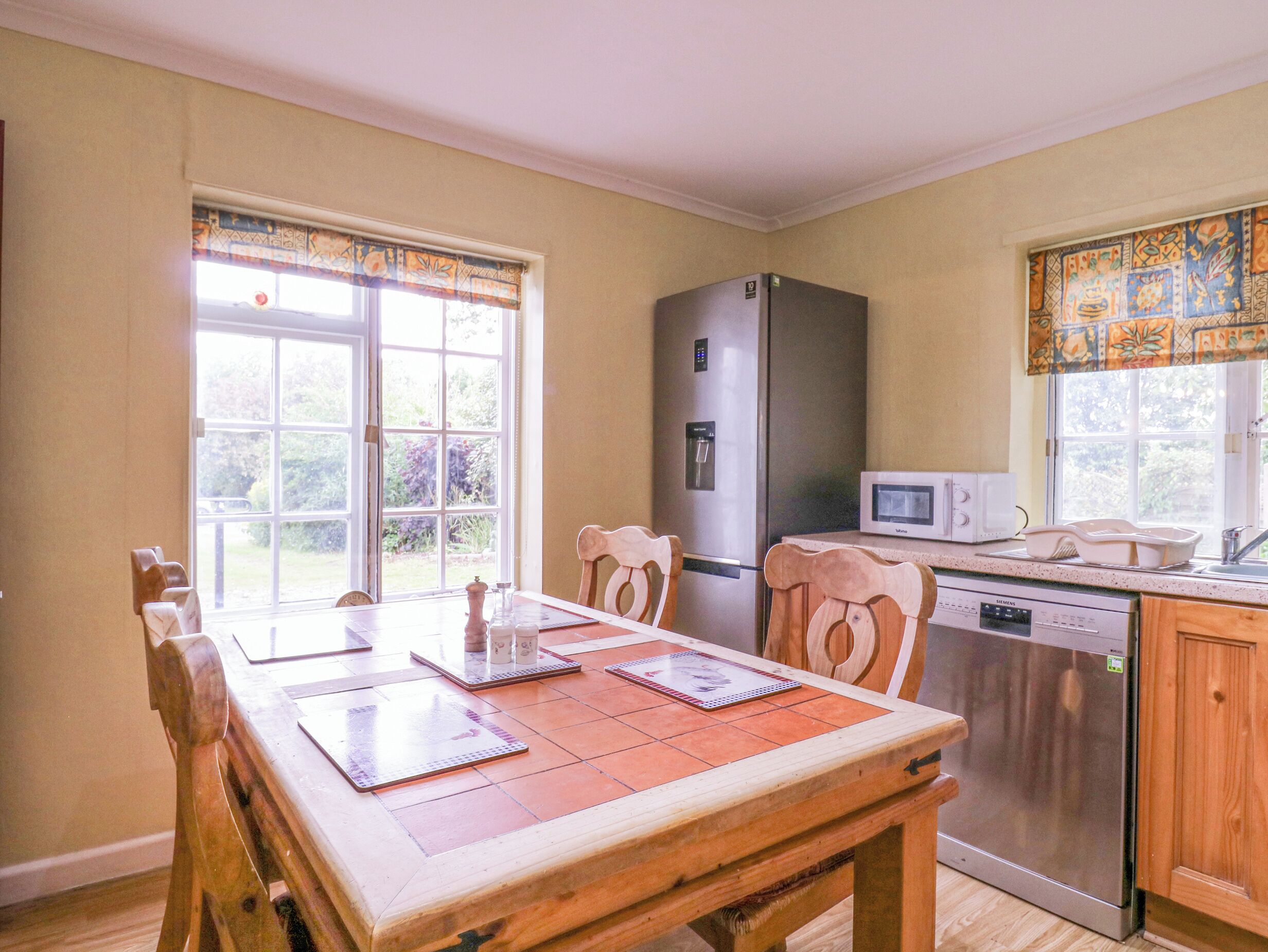 Una cocina con una mesa de madera, sillas, un refrigerador, un microondas y un lavavajillas.