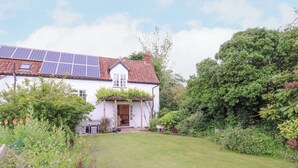 Une maison blanche avec un toit recouvert de tuiles rouges, des panneaux solaires et un jardin où poussent différentes espèces de plantes.