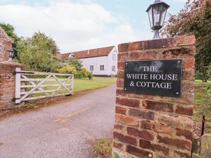 A sign for "The White House & Cottage" with a brick wall and a white gate leading to a building with a red-tiled roof. - White House Cottage (Fakenham)
