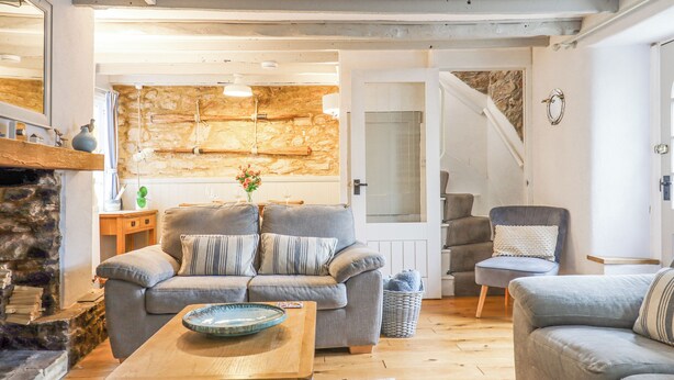 A cozy living room with a grey sofa, a wooden coffee table, and a stone fireplace. - 3 Pebble Cottage (Brixham)