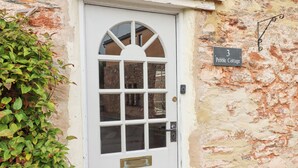 A white door with a glass panel and a small window above it, set in a stone wall. A sign above the door reads "3 Pebble Cottage." - 3 Pebble Cottage (Brixham)