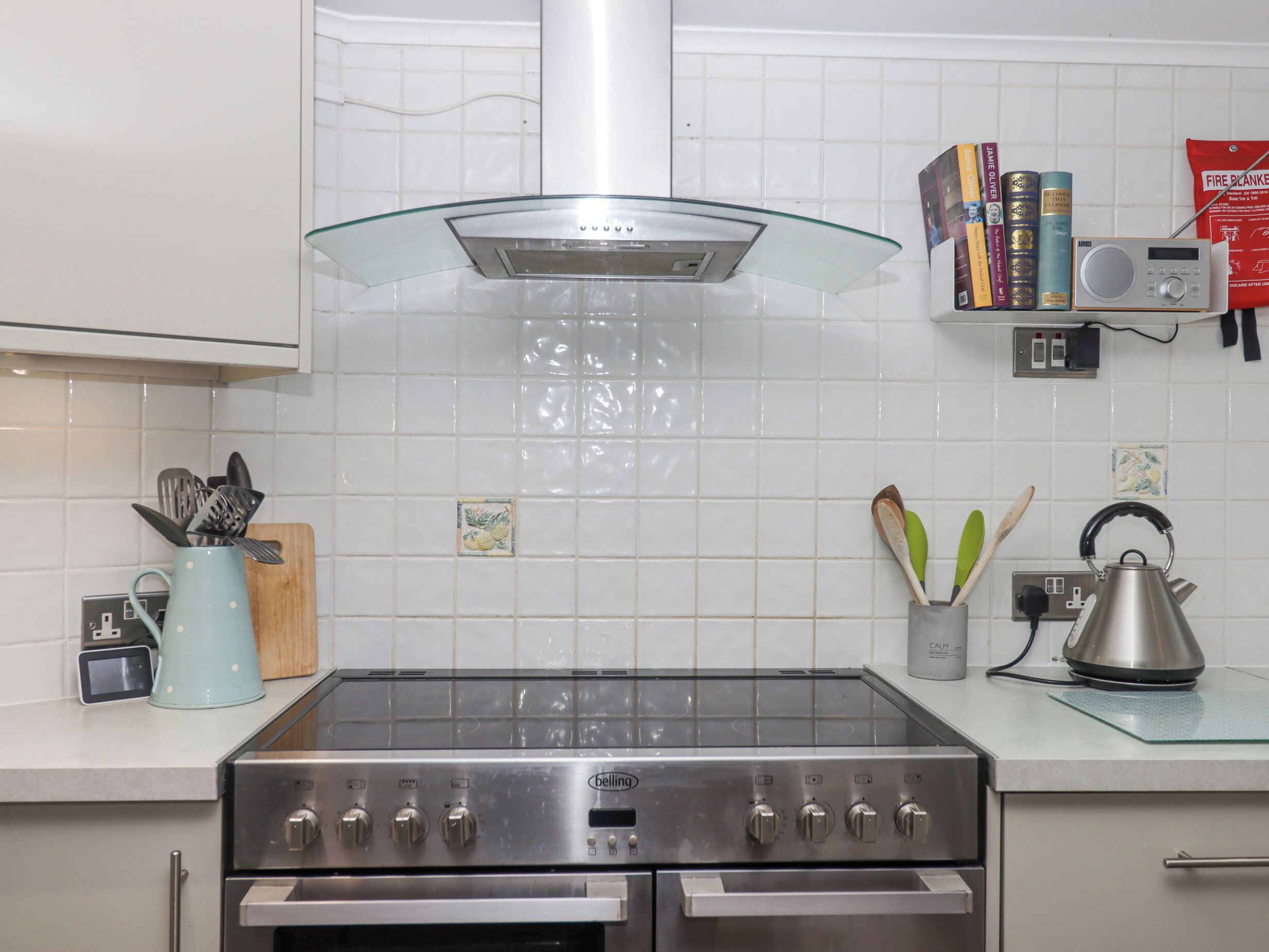 A modern kitchen with a stainless steel stove, a glass hood, and a white tiled backsplash.