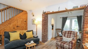 A cozy living room with a wooden staircase, a dark blue sofa with yellow cushions, a plaid armchair, and a small wooden table with a cup and saucer. - Miller's Cottage (Dorchester)