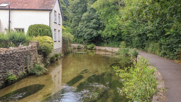 A narrow waterway flanked by lush greenery and a traditional building with a tiled roof. - Miller's Cottage (Dorchester)
