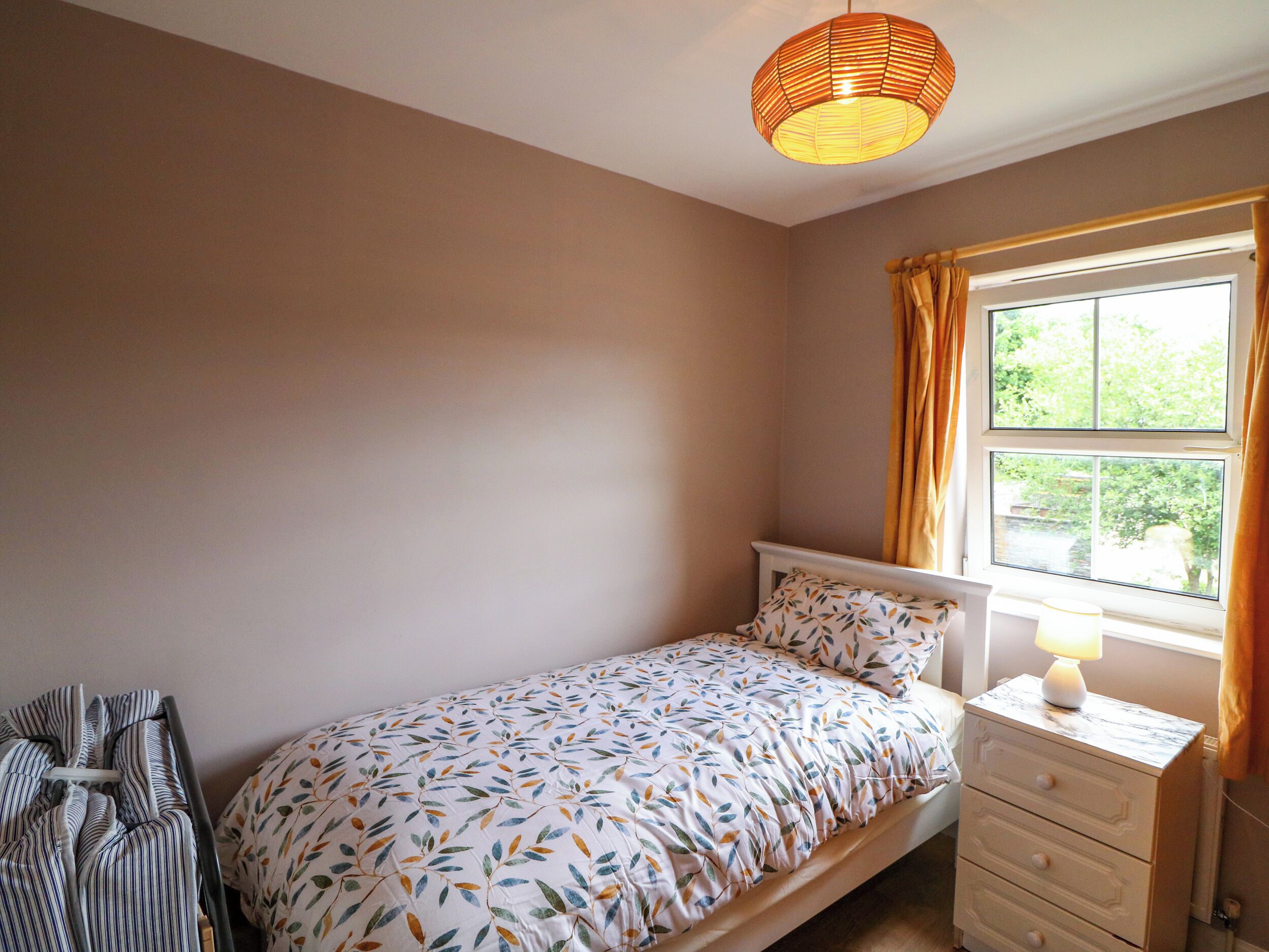 Un dormitorio con una cama individual, una mesita de noche con lámpara, una ventana con cortinas y una silla.