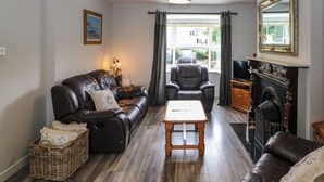 A living room with a leather sofa, a wooden coffee table, a fireplace, and a large mirror. - 23 Cois Caol (Skibbereen)
