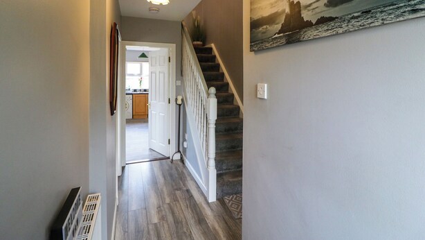 A hallway with a staircase, a painting of a lighthouse, and a door leading to a kitchen. - 23 Cois Caol (Skibbereen)