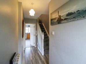 A hallway with a staircase, a painting of a lighthouse, and a door leading to a kitchen. - 23 Cois Caol (Skibbereen)