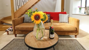 Een woonkamer met een bruine bank, een glazen vaas met zonnebloemen en een fles Moët & Chandon champagne op een ronde houten tafel.