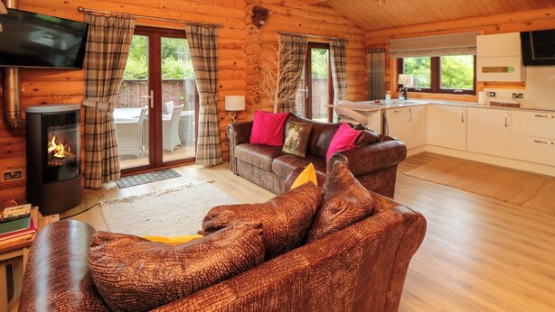 A cozy cabin interior with a fireplace, a sofa, a dining area, and a kitchen. - Baysdale Lodge 5 (Middlesbrough)
