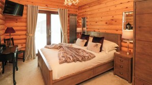 A log cabin bedroom with a large bed, wooden headboard, bedside tables, a TV mounted on the wall, and a chandelier. - Baysdale Lodge 5 (Middlesbrough)