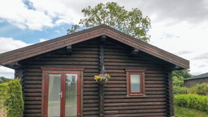 A log cabin with a front porch, a window, and a hanging flower basket. - Baysdale Lodge 5 (Middlesbrough)