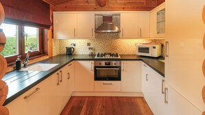 Cocina con gabinetes de madera, estufa, microondas y ventana con vista a la vegetación.