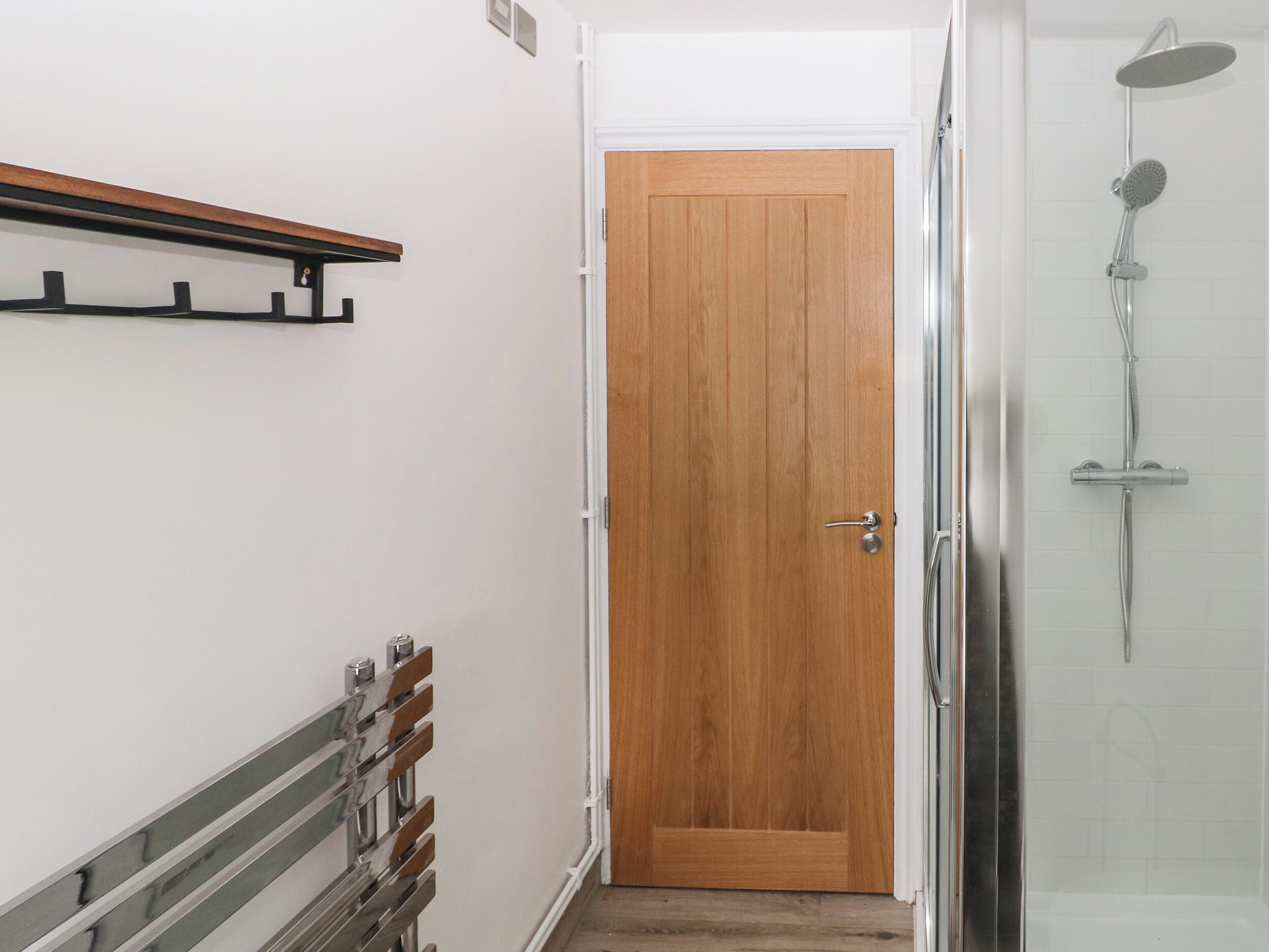 A bathroom with a shower, a wooden door, and a towel rack.