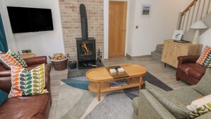 A living room with a fireplace, leather sofas, a coffee table, and a TV. - Folly Cottage (Narberth)