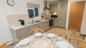 A modern kitchen with a dining table set for four, featuring a clock on the wall. - Folly Cottage (Narberth)