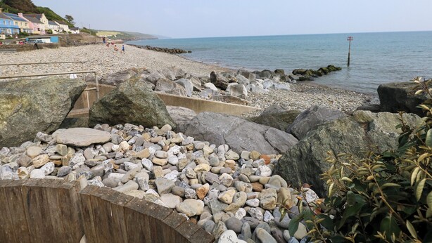 A rocky beach with a wooden walkway leading to the sea, houses in the background, and a clear sky. - Folly Cottage (Narberth)