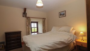 A bedroom with a bed, a nightstand, a dresser, a window with curtains, and a ceiling light. - Ereiniog 2 (Garndolbenmaen)