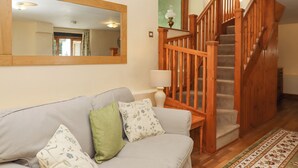 Ein Wohnzimmer mit einer Holztreppe, einer Couch mit Kissen, einer Lampe und einem Spiegel an der Wand.