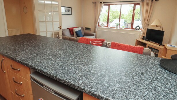 A kitchen with granite countertops, a dining area with a table and chairs, a television, and a window with curtains. - Valley View (Cleator Moor)