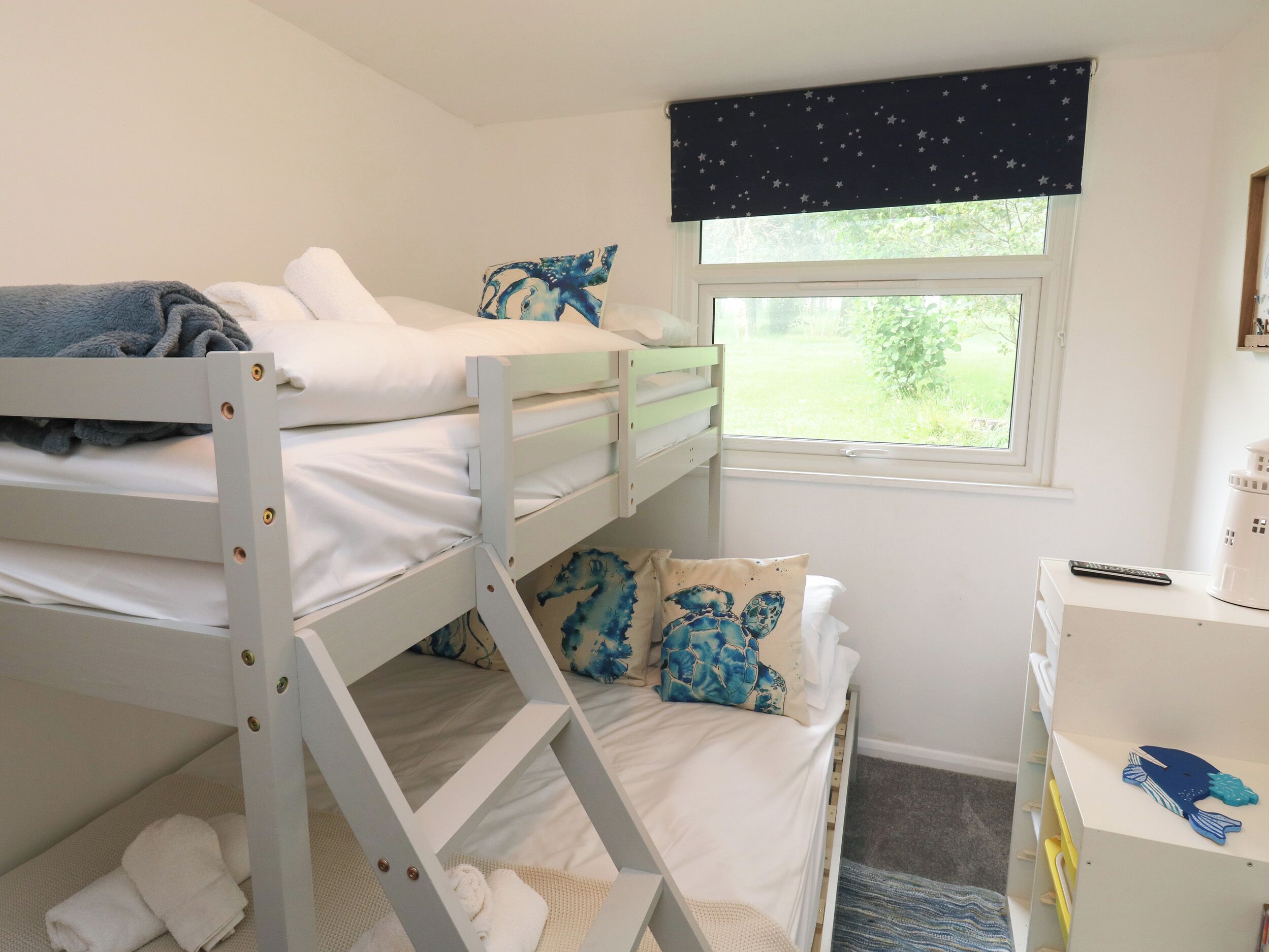 A bunk bed room with a window, a desk with a computer, and a bookshelf.