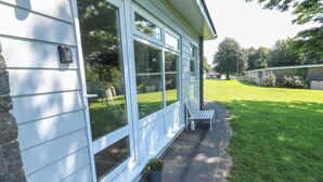 A covered porch with a bench, a small garden area with potted plants, and a clear view of the surrounding lawn and trees. - 61 Norton Park (Dartmouth)
