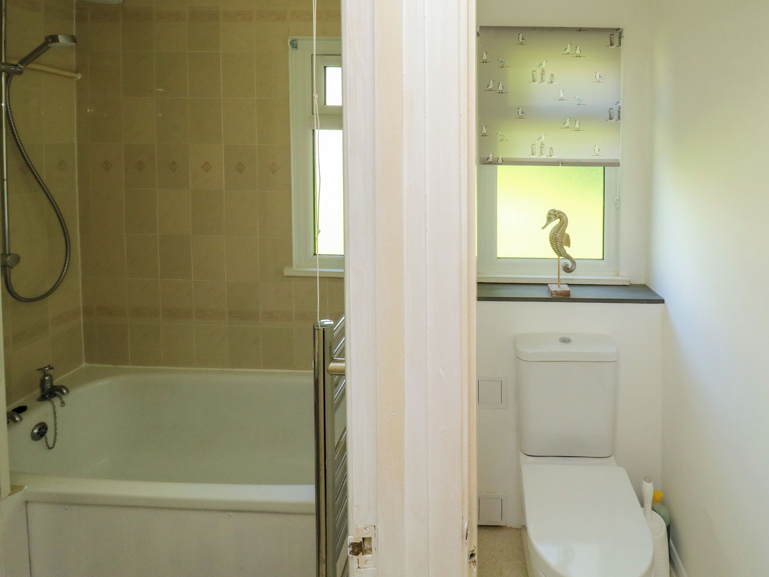Ein Badezimmer mit Badewanne, Toilette und einem Fenster mit einer Seepferdchen-Dekoration.