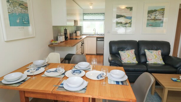 A compact living space with a dining area, kitchen, and a seating area with a black leather sofa. - 61 Norton Park (Dartmouth)