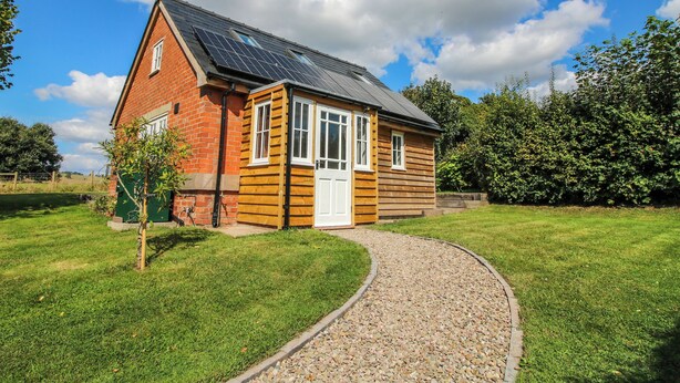 A single-story house with a sloped roof, a brick exterior, and a small front porch. - Rose Cottage (Hereford)