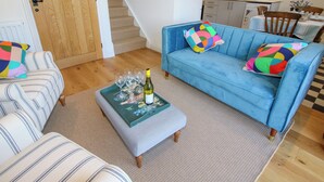 A living room with a blue sofa, striped armchairs, a coffee table with wine glasses, and a staircase leading to another room. - Rose Cottage (Hereford)