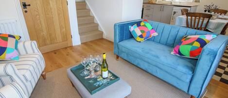 Una sala de estar con un sofá azul, sillones a rayas, una mesa de centro con copas de vino y una escalera que conduce a otra habitación.