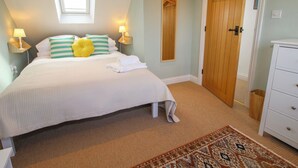 A neatly made bed with pillows, a bedside lamp, a wooden door, and a small white dresser. - Rose Cottage (Hereford)