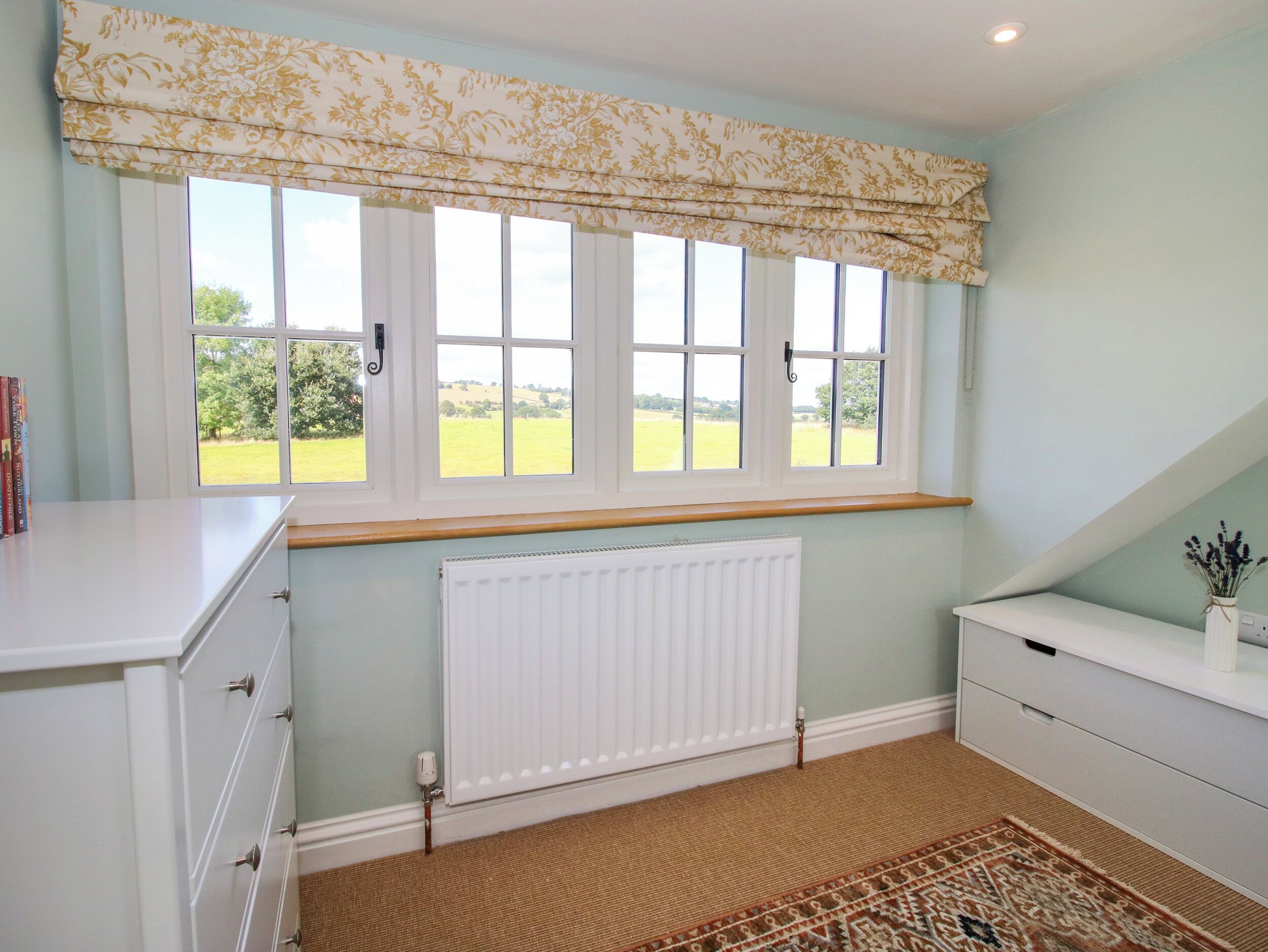 Une pièce avec une grande fenêtre, un radiateur, une armoire blanche et un tapis à motifs.