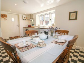 A dining area with a checkered floor, a table set for four with floral tablecloths, and a window with a view of buildings. - Rose Cottage (Hereford)