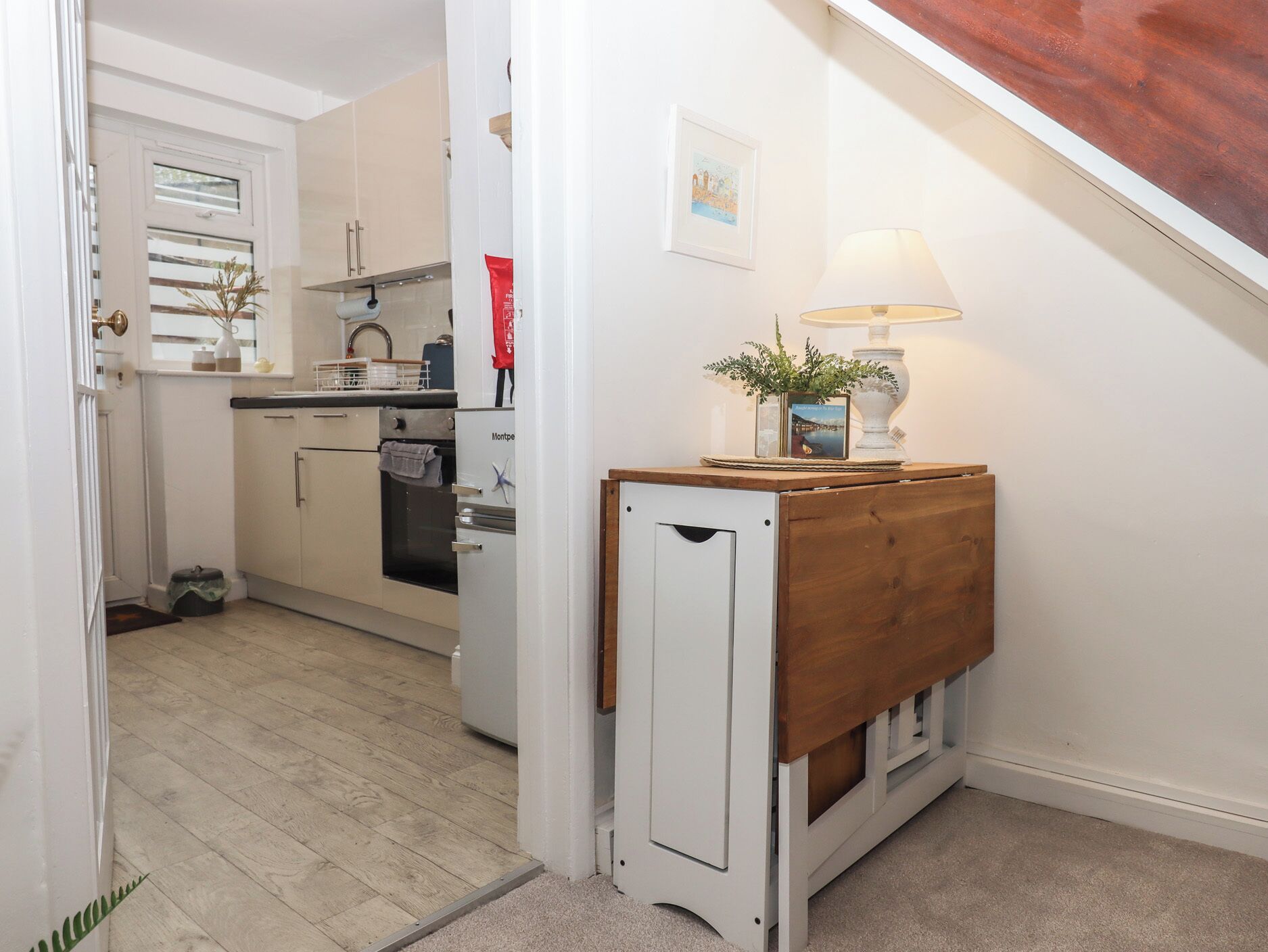 A kitchen with white cabinets, a refrigerator, and a wooden bench with a lamp.