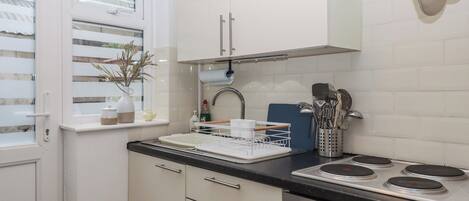 A kitchen with white cabinets, a black countertop, a stove, and a window with blinds.