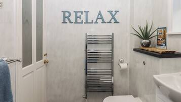 A bathroom with a white toilet, a towel rack, a towel, a shower with a glass door, and a sign that says "RELAX".