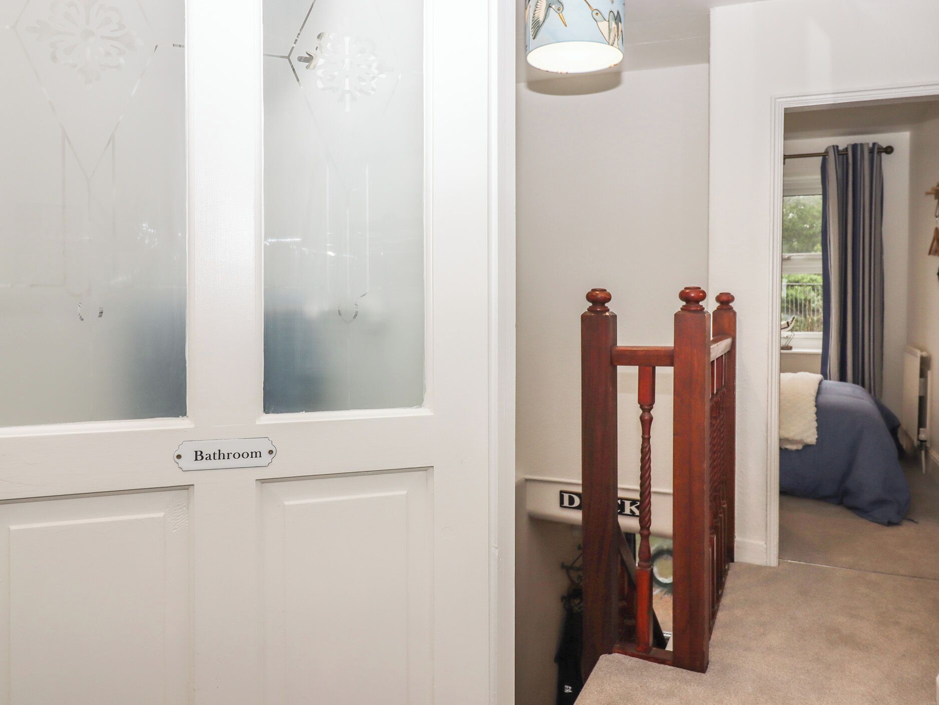 A staircase leading to a bedroom with a bed, a window with curtains, and a door labeled "Bathroom".