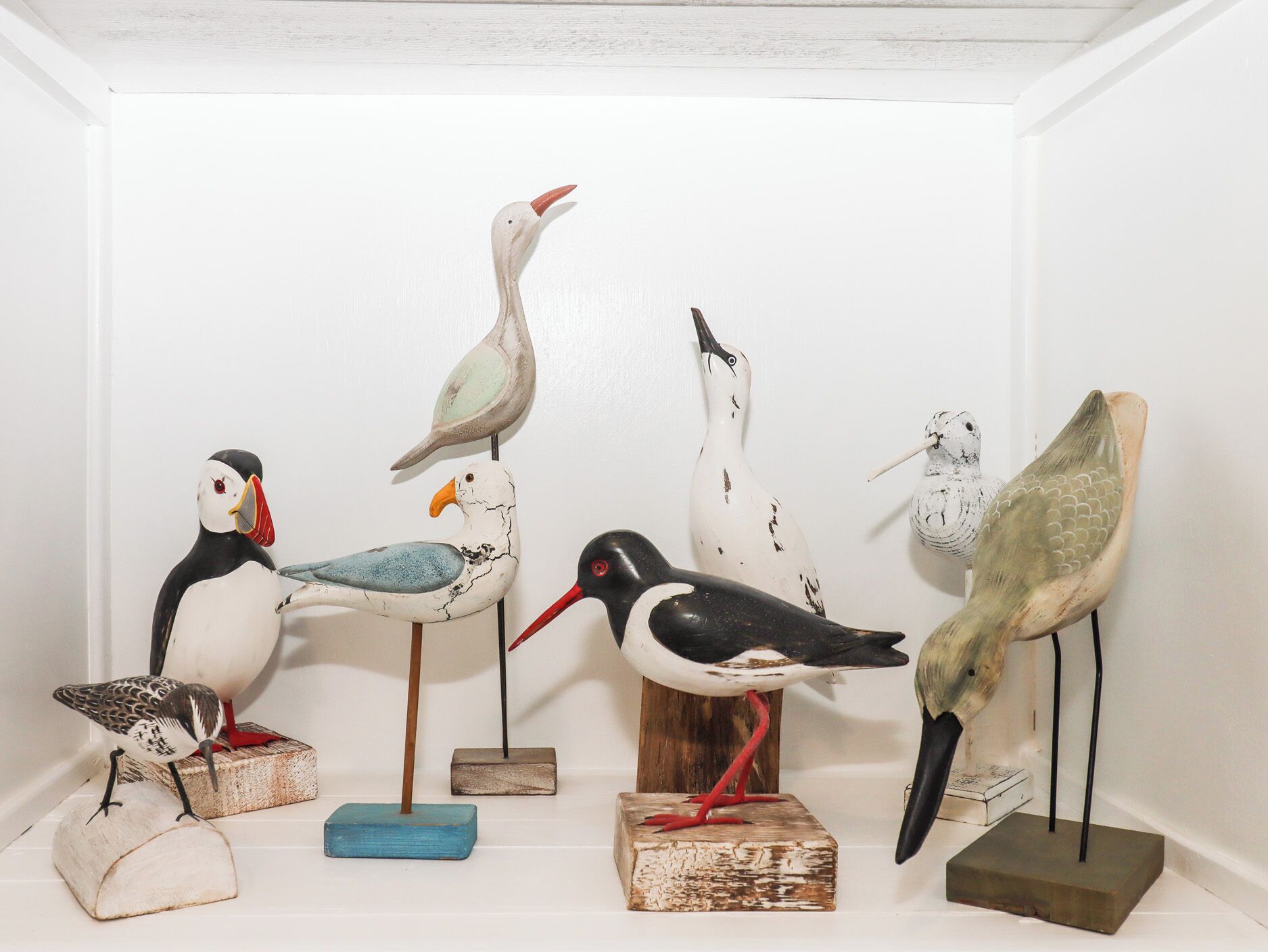 Eine Sammlung aus Vogelskulpturen auf Holzwürfeln vor einer weißen Wand.
