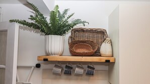 A kitchen shelf with a potted plant, a woven basket, a ceramic pitcher, and hanging kitchen utensils. - Pie Cottage (Teignmouth)