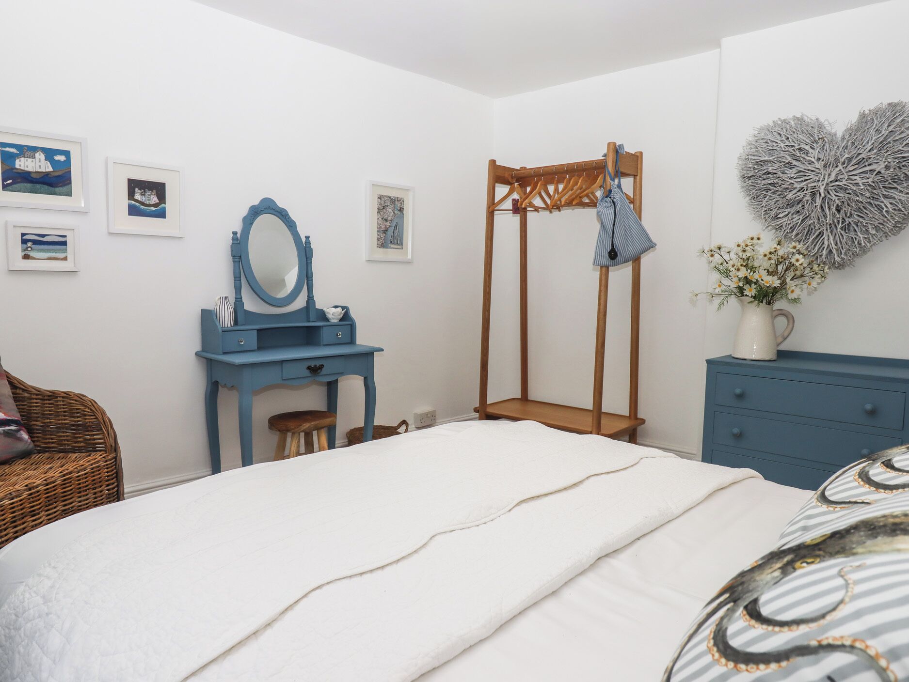 Una camera da letto con un letto, una cassettiera blu, un armadio in legno, una toeletta blu con uno specchio e decorazioni murali.