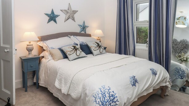 A bedroom with a bed, two bedside tables, star decorations, and a window with curtains. - Pie Cottage (Teignmouth)