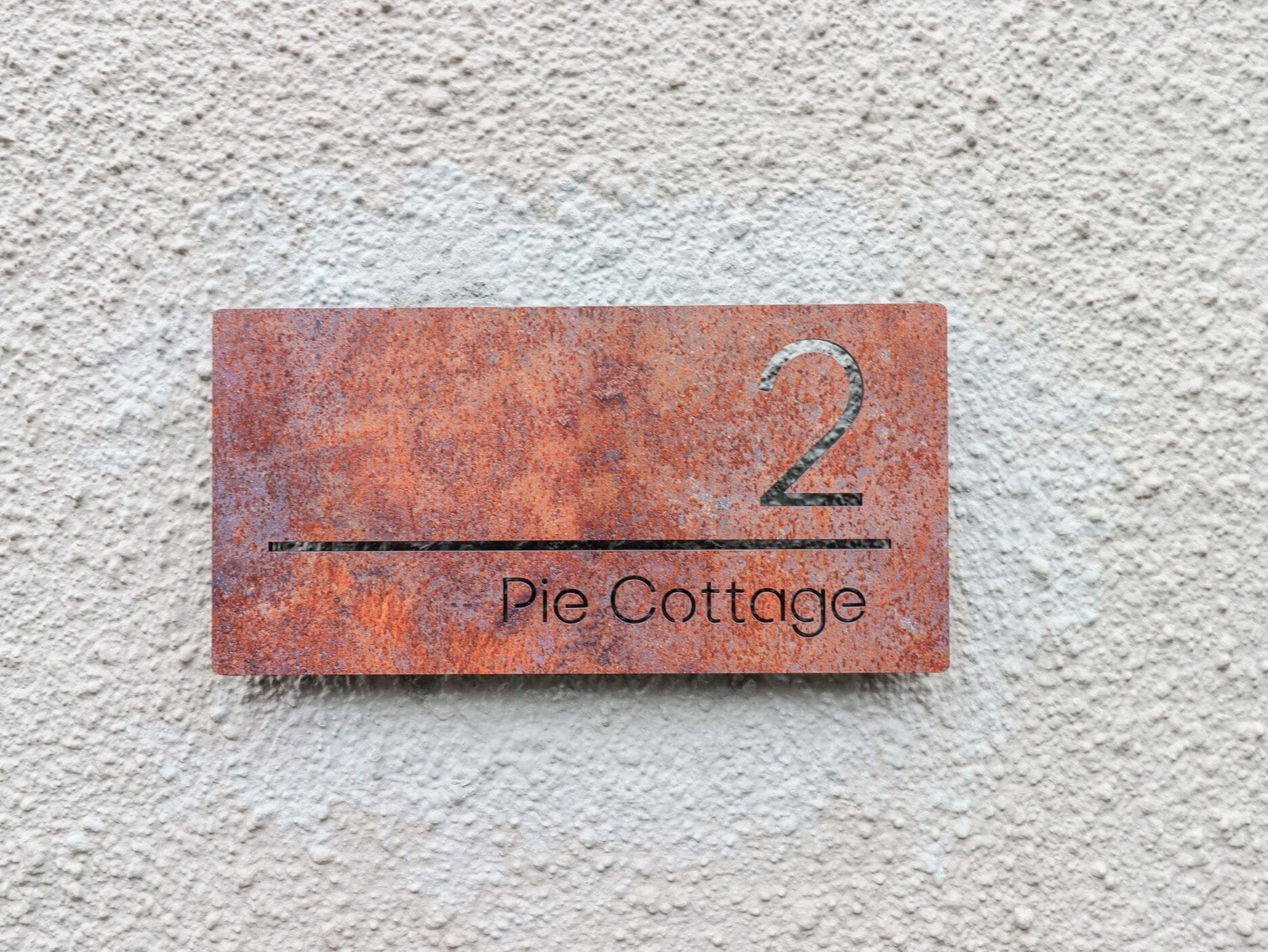 A metal plaque with the number 2 and the words "Pie Cottage" on a textured wall.