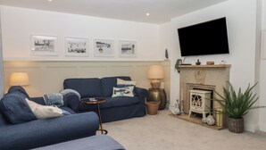 A living room with a sofa, a small side table, a lamp, a fireplace, and framed pictures on the wall. - Pie Cottage (Teignmouth)