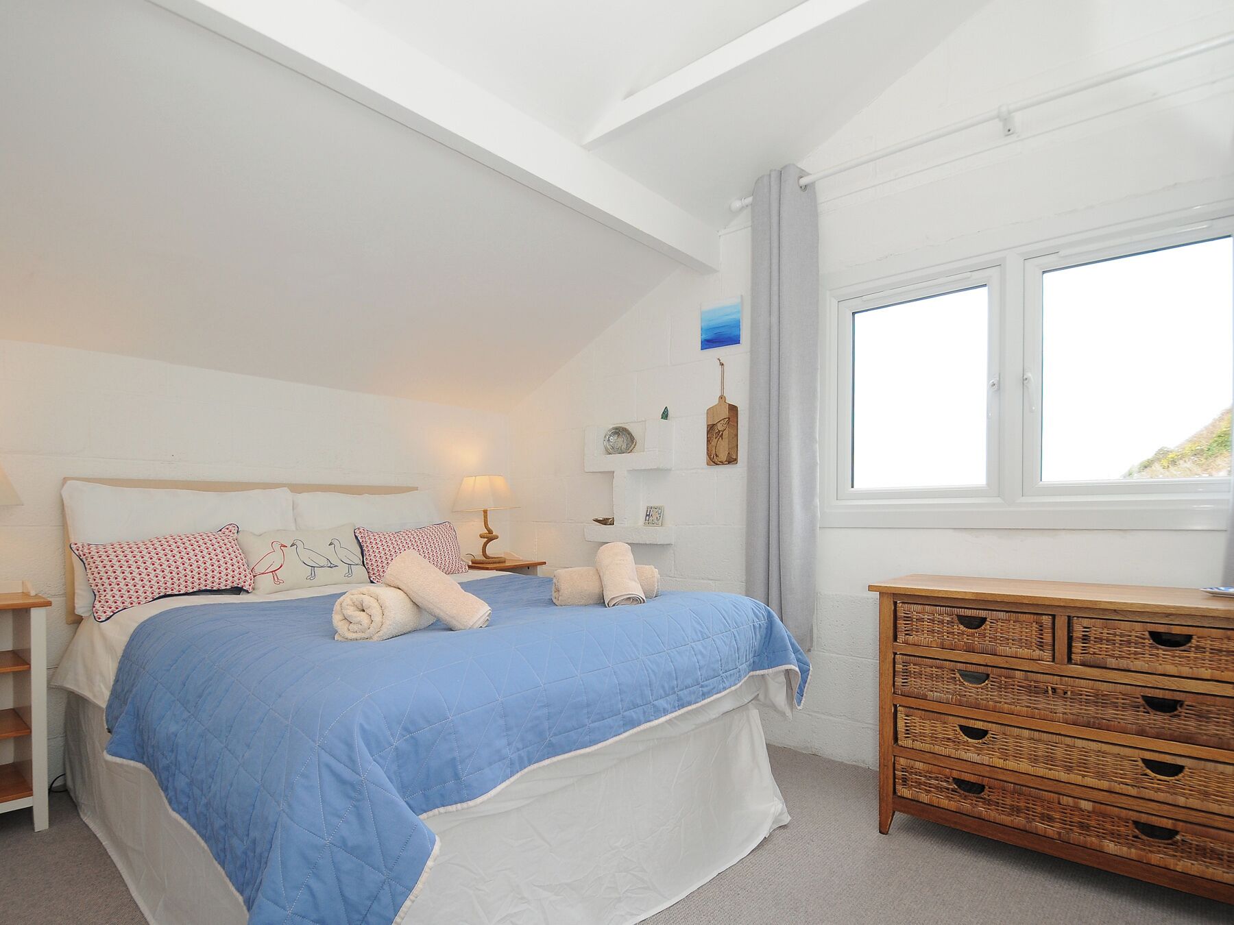 Une chambre à coucher comprenant un lit, des tables de chevet, une commode et une fenêtre donnant sur un beau paysage.