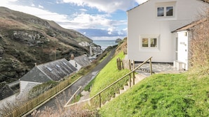A coastal house with a steep driveway leading to a white exterior, overlooking the sea and a rocky hillside.